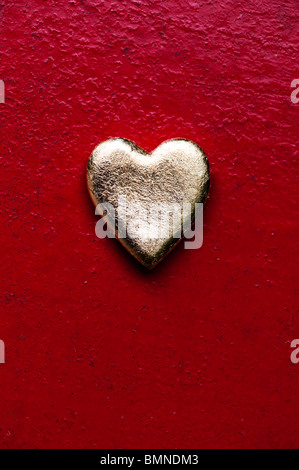 Forme de coeur en or contre texture rouge metal fond peint Banque D'Images