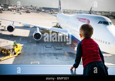 Un jeune garçon portant une chemise rouge et bleu regarder par une fenêtre sur la piste de l'aéroport d'Heathrow Terminal 5 Banque D'Images