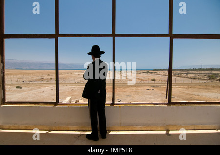 Un juif religieux ultra-orthodoxe pairs hors de la fenêtre de l'hôtel Lido déserte complexe dans la rive nord de la Mer Morte. Israël Banque D'Images