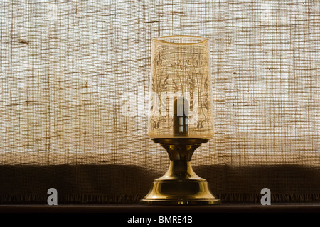 Vieille lampe bougie sur windowboard contre fenêtre couverte de Hesse Banque D'Images