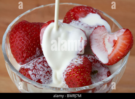 Verser la crème fraîche réel au-dessus d'un bol de fraises fraîches et crème au Royaume-Uni Banque D'Images