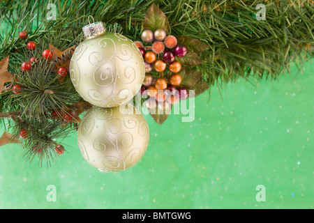 Défilement d'or Boule de Noël avec des baies de houx, fond vert et copyspace Banque D'Images