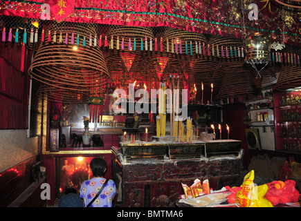 Cône d'encens, joss-stick, statue d'or de l'intérieur de la Kwun Yam Temple, avec deux dames chinoises en prière, Sheung Wan, Hong Kong Banque D'Images