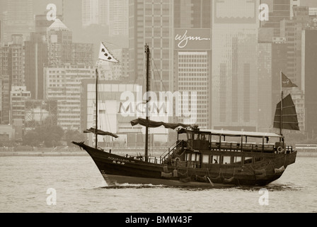 Dans le port de Victoria, une jonque classic sails en face de l'horizon de Hong Kong et les gratte-ciel que la ligne de cette ville historique. Banque D'Images