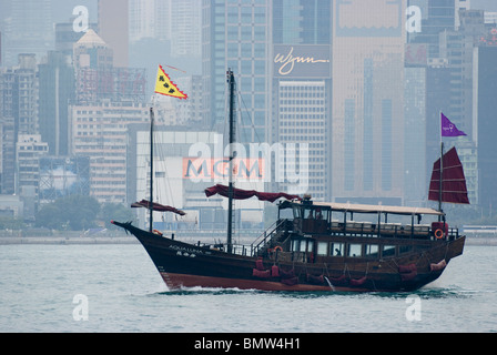 Dans le port de Victoria, une jonque classic sails en face de l'horizon de Hong Kong et les gratte-ciel que la ligne de cette ville historique. Banque D'Images