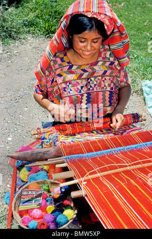 Une jeune fille Maya tisse avec les schémas traditionnels de tissu coloré sur son métier à la maison à l'extérieur près du lac Atitlan, Guatemala. Banque D'Images