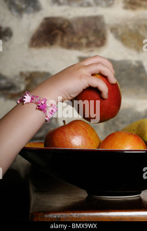 Stock photo d'une petite filles part atteignant jusqu'à prendre un apple hors de la corbeille de fruits. Banque D'Images