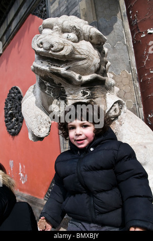 A cute Young boy chinois avec un lion en pierre en face d'un temple. Banque D'Images