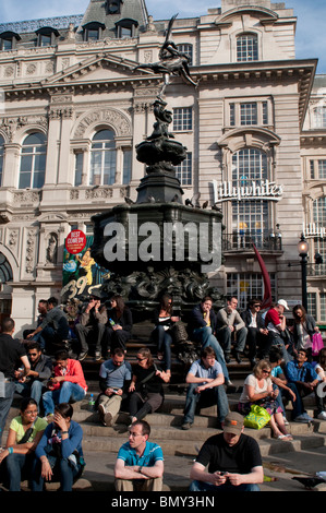 Les gens assis autour de la statue d'Eros à Piccadilly Circus, Londres W1, UK Banque D'Images