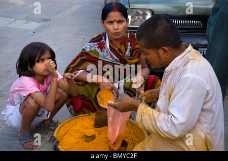 Un homme vend curcuma poudre orange à une femme et sa fille à Durbar Square, Katmandou, Népal. Banque D'Images