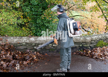 Un homme à l'aide d'un leafblower pour effacer les feuilles d'automne d'une route Banque D'Images