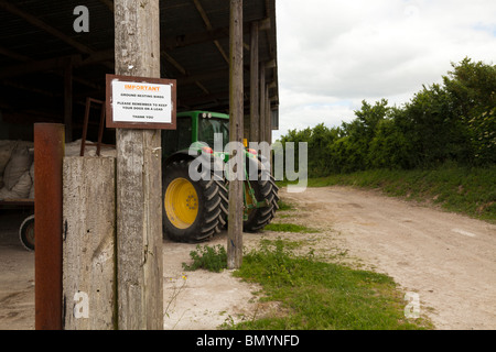 Inscrivez-vous sur alerte de bâtiments agricoles les promeneurs à maintenir les chiens en laisse avec le tracteur en arrière-plan Banque D'Images