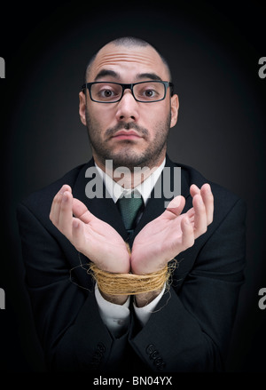 Un homme sur un costume montre ses mains attachées avec une expression perplexe. Banque D'Images