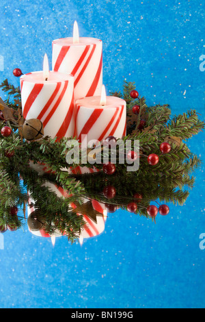 Trois rayures rouge et blanc bougies de Noël avec des réflexions, des feuilles, des baies, Rusty bells et copyspace Banque D'Images