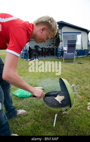 Jeune homme Cuisiner les poissons sur un barbecue en camping et carvanning à Cornwall Banque D'Images