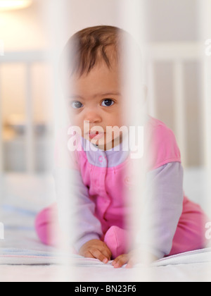 Sept mois, cute baby girl sitting dans un lit d'enfant derrière les barreaux