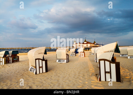 Chaises de plage à capuchon sur une plage de sable fin, jetée d'Ahlbeck en arrière-plan, Usedom, Allemagne Banque D'Images