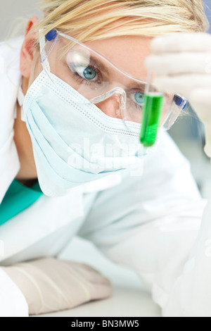 Un chercheur scientifique ou médicale blonde ou le médecin à tube à essai de solution verte dans un laboratoire portant des lunettes de sécurité Banque D'Images