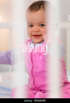 Sept mois, Cute smiling baby girl sitting à l'intérieur d'un lit-bébé Banque D'Images