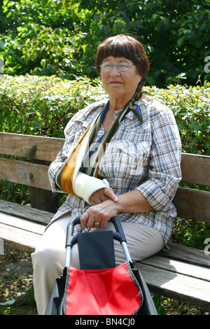 Pensionné femme avec le bras en écharpe sur banc de parc reste sur le banc de parc Banque D'Images