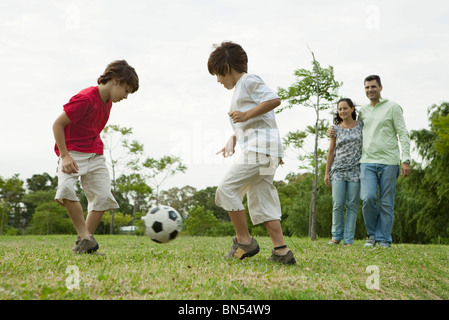 Garçons jouant au football, les parents à regarder en arrière-plan Banque D'Images