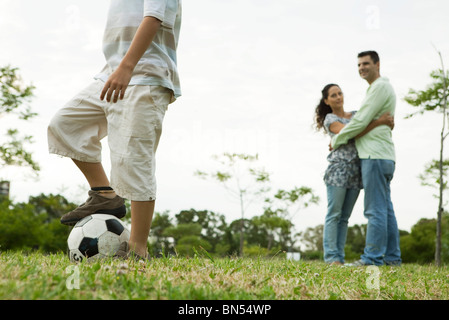 Boy Playing with soccer ball, parents et embrassant en arrière-plan Banque D'Images