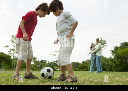 Garçons jouant au football, les parents adoptant en arrière-plan Banque D'Images