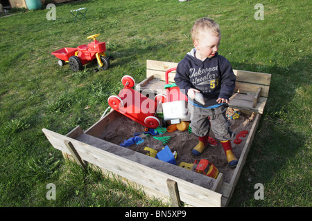 Bébé garçon dans le jardin jouer dans un bac à sable avec des jouets en plastique PARUTION MODÈLE Banque D'Images