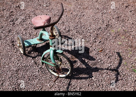 Tricycle classique antique rouillé pour enfants sur un chemin de gravier Banque D'Images