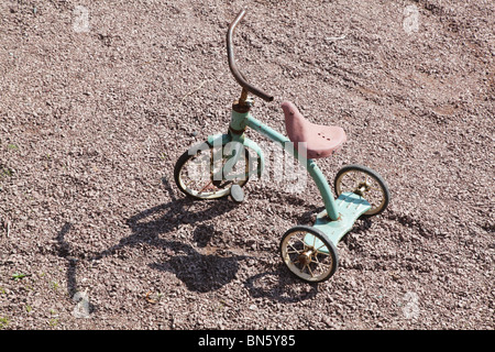 Tricycle classique antique rouillé pour enfants sur un chemin de gravier Banque D'Images