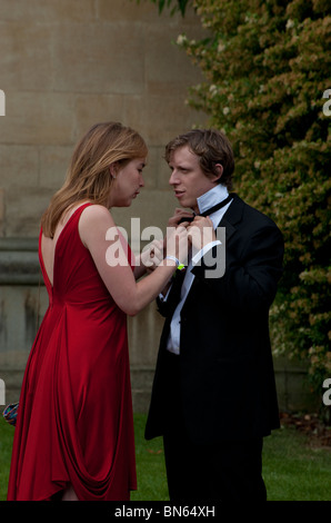 Une femme blonde dans une robe de soirée rouge contribue à sa date avec son nœud papillon à l'extérieur de la balle Wadham College à Oxford. Banque D'Images