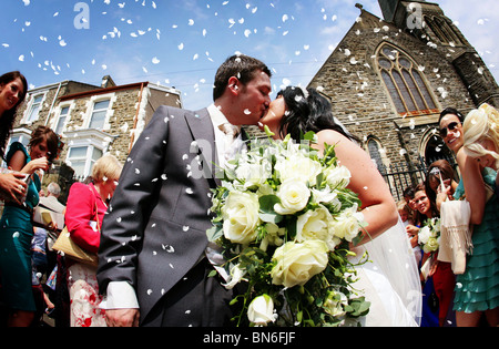 Bride and Groom kissing sous les confettis lancés par les invités du mariage à l'extérieur d'une église sur leur grand jour mariage spécial Banque D'Images