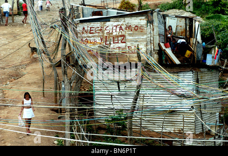 Une fille marche sur une rue non pavée où un labyrinthe de lignes électriques illégaux dans un bidonville de Caracas, Venezuela. Banque D'Images