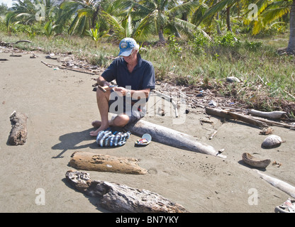 Aplatissement touristique mâle et boîtes de conserve, les aidant à se débarrasser des déchets et ordures jonchent cette belle plage sur Mamitupu. Banque D'Images