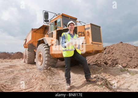 Hispanic construction worker with blueprints près de dump truck Banque D'Images