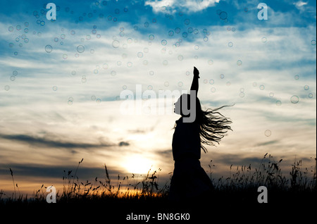 Jeune fille énergique s'amusant de sauter et attraper des bulles au coucher du soleil. Silhouette Banque D'Images