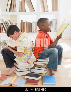 Garçons assis sur des piles de livres et lecture Banque D'Images