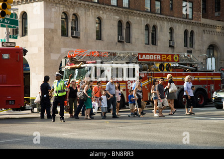 Passant et les premiers intervenants sur les lieux d'un trou de feu sur West 23rd Street dans le quartier de Chelsea à la mode de New York Banque D'Images