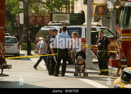 Passant et les premiers intervenants sur les lieux d'un trou de feu sur West 23rd Street dans le quartier de Chelsea à la mode de New York Banque D'Images