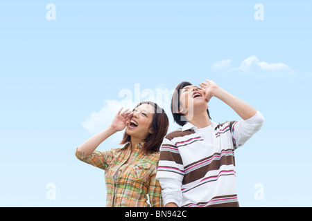 Jeune homme et femme criant sous ciel bleu Banque D'Images