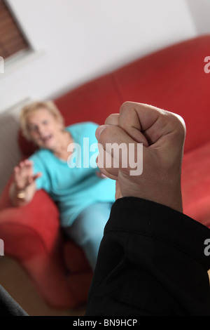 Poing mâle soulevée visant vers une vieille femme assise sur un canapé à la maison Banque D'Images