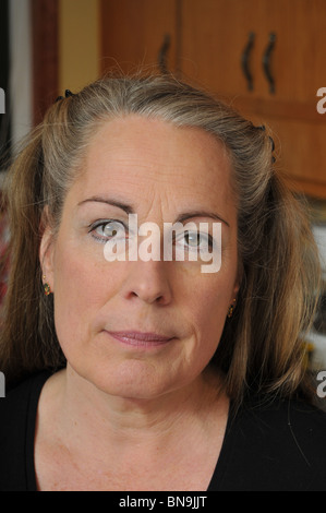 Femme d'âge moyen standing dans la cuisine en face d'armoires. Banque D'Images