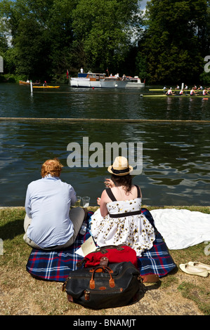 Un couple, un homme et une femme assis sur un tapis de pique-nique sur la berge de la Tamise bénéficiant d'Henley Royal Regatta. Banque D'Images