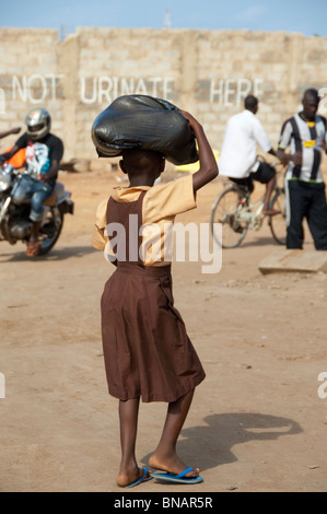 L'Afrique, Ghana, Accra. Marché de l'artisanat et du textile d'Accra. Écolière avec sac sur sa tête en face de 'ne pas uriner ici'. Banque D'Images