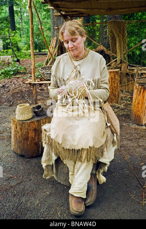 Un interprète vêtu comme un Indien Powhatan tisse un panier de paille pour montrer aux visiteurs la vie dans le début des années 1600, à Jamestown Settlement, New York, USA. Banque D'Images