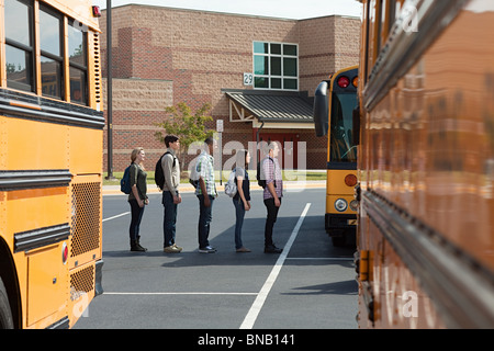 Les élèves du secondaire d'attente pour les autobus scolaires Banque D'Images