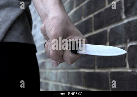 Main d'un jeune homme tenant un couteau en passant devant un mur de briques Banque D'Images