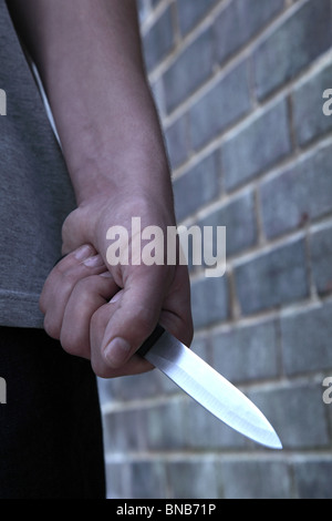 Main d'un jeune homme tenant un couteau en passant devant un mur de briques Banque D'Images