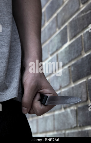 Main d'un jeune homme tenant un couteau en passant devant un mur de briques Banque D'Images