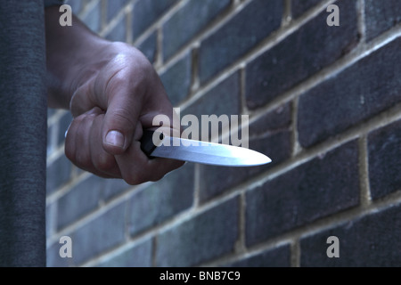 Main d'un jeune homme tenant un couteau en passant devant un mur de briques Banque D'Images